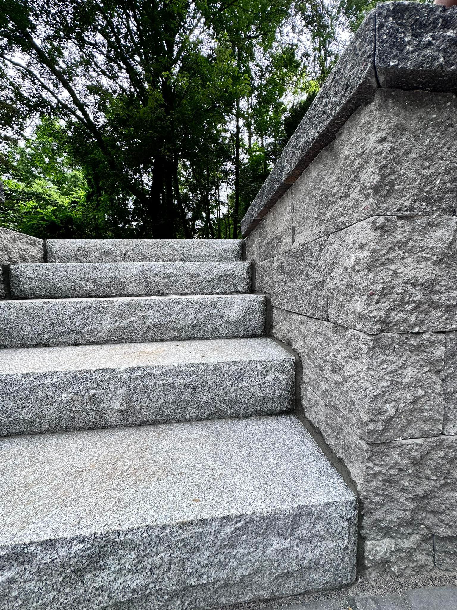 a set of stairs made of granite next to a stone wall .