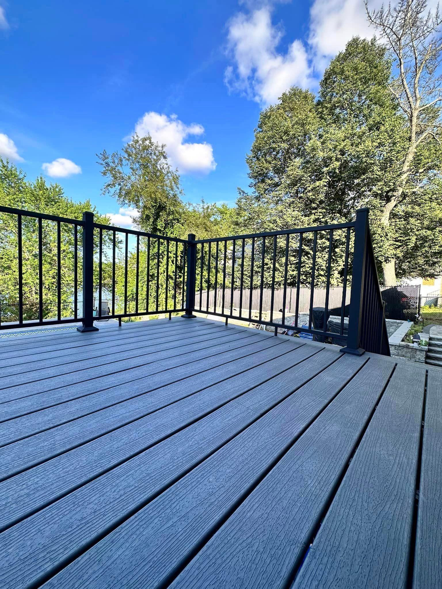 a wooden deck with a metal railing and trees in the background .