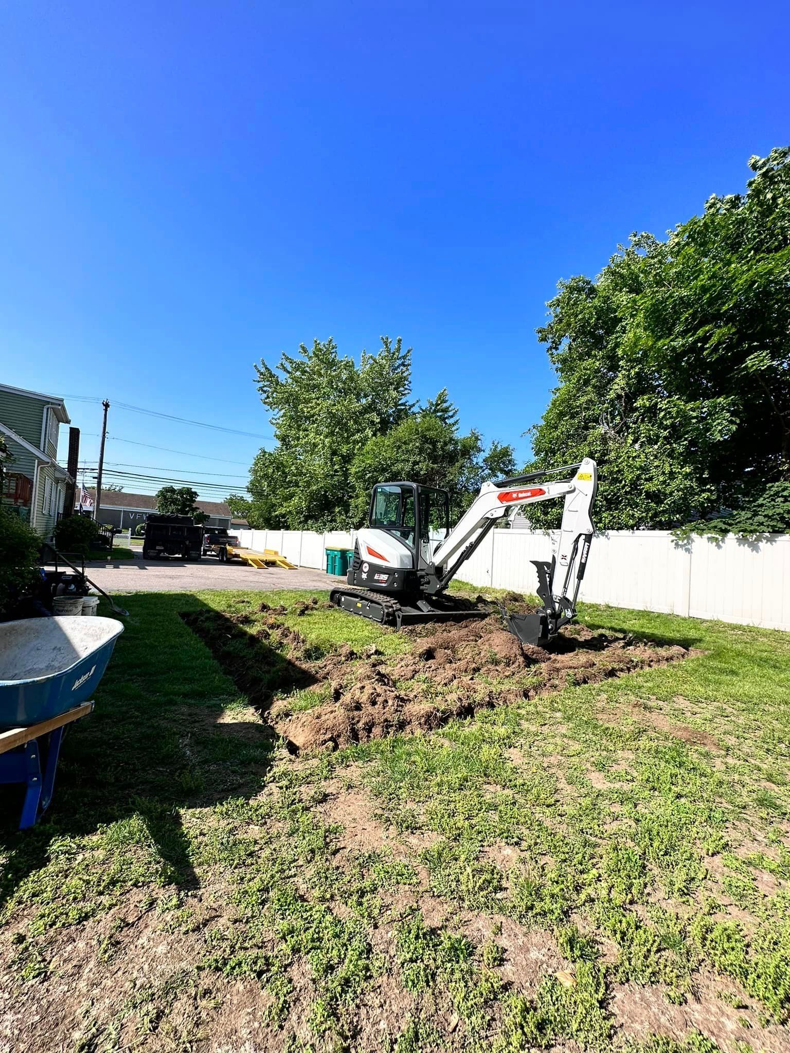 a man is using an excavator to dig a hole in the ground in a backyard .