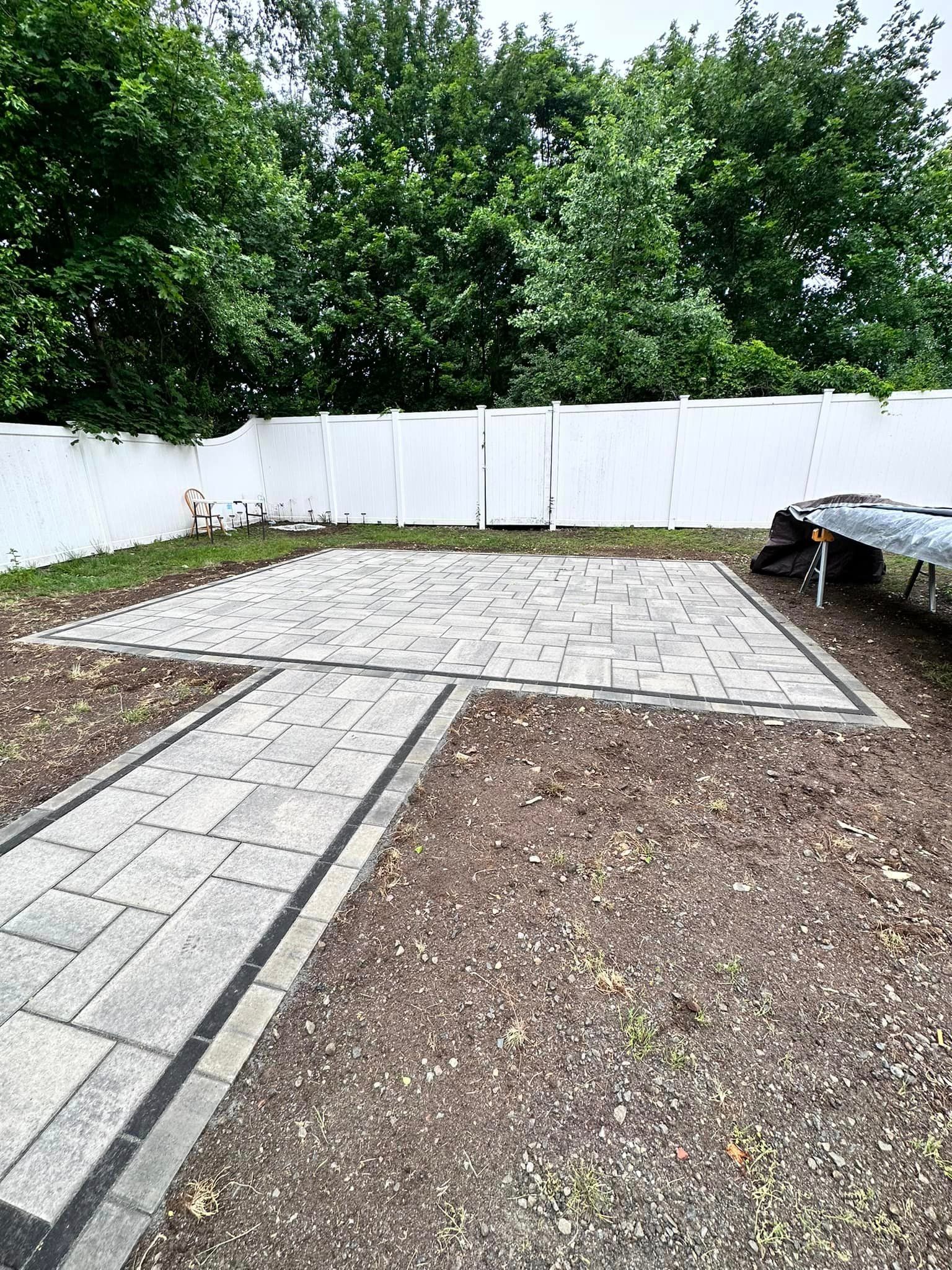 a backyard with a brick walkway and a white fence .