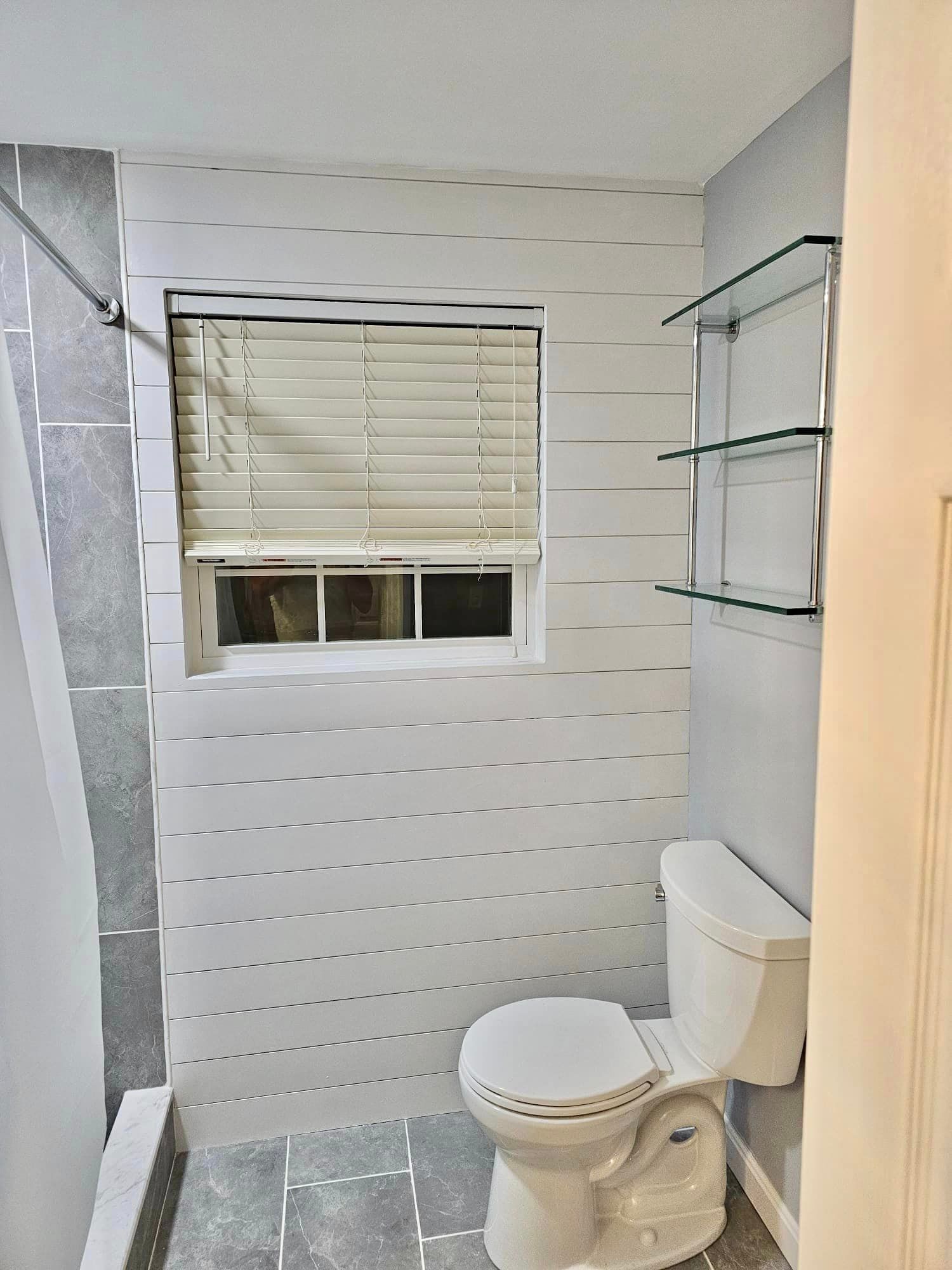 a bathroom with a toilet , window and shelves .