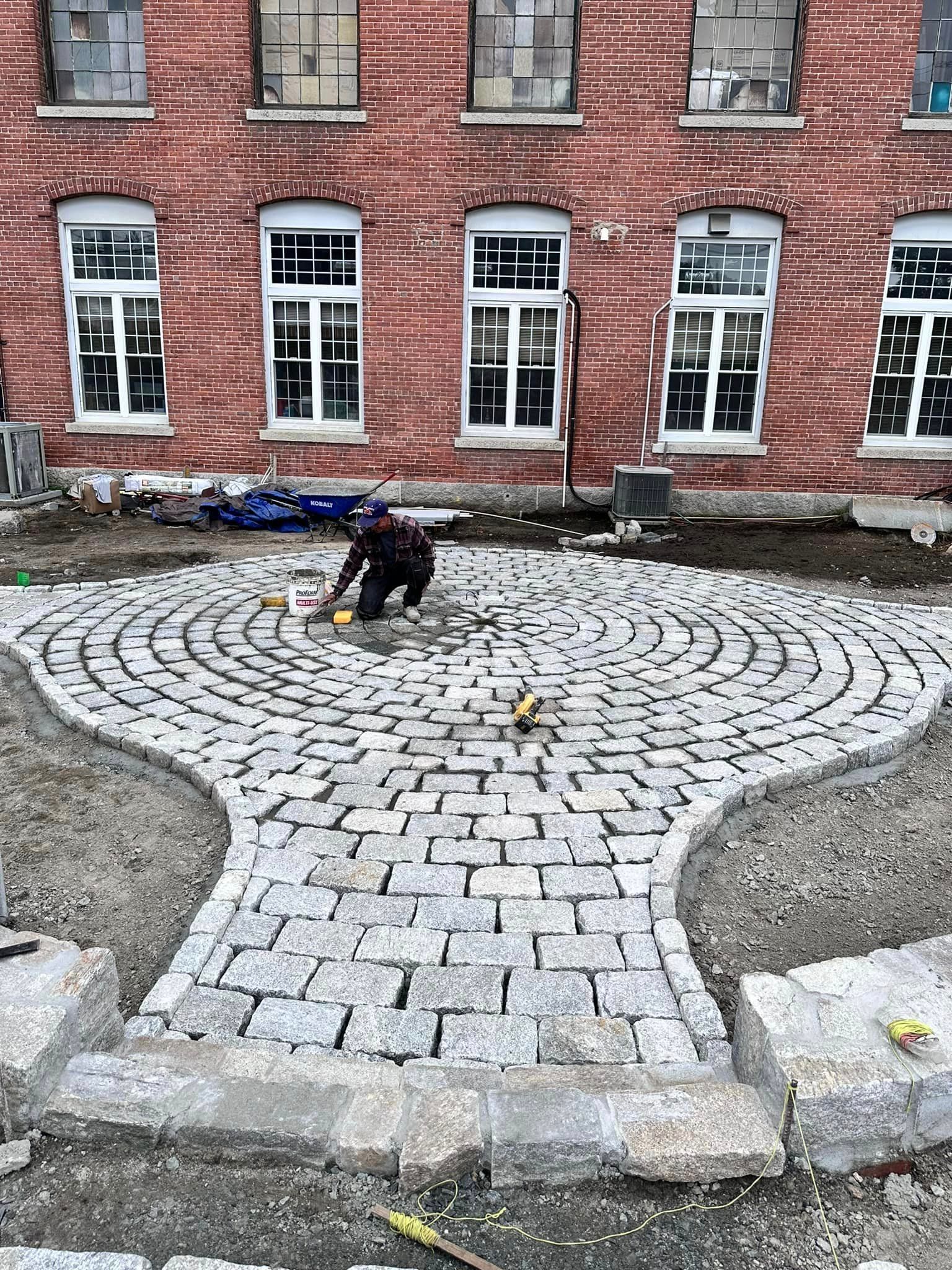 a man is working on a brick walkway in front of a brick building .
