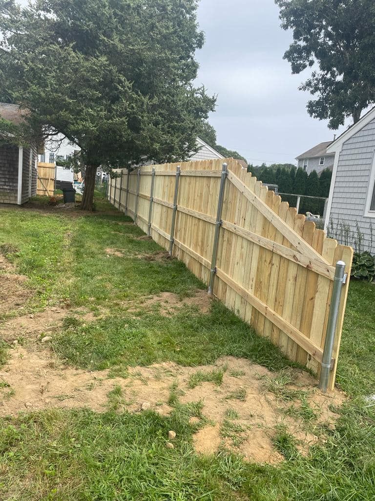 a wooden fence is sitting in the middle of a grassy yard next to a house .
