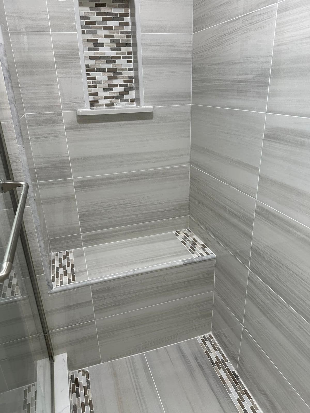a bathroom with gray tiles and a walk in shower .
