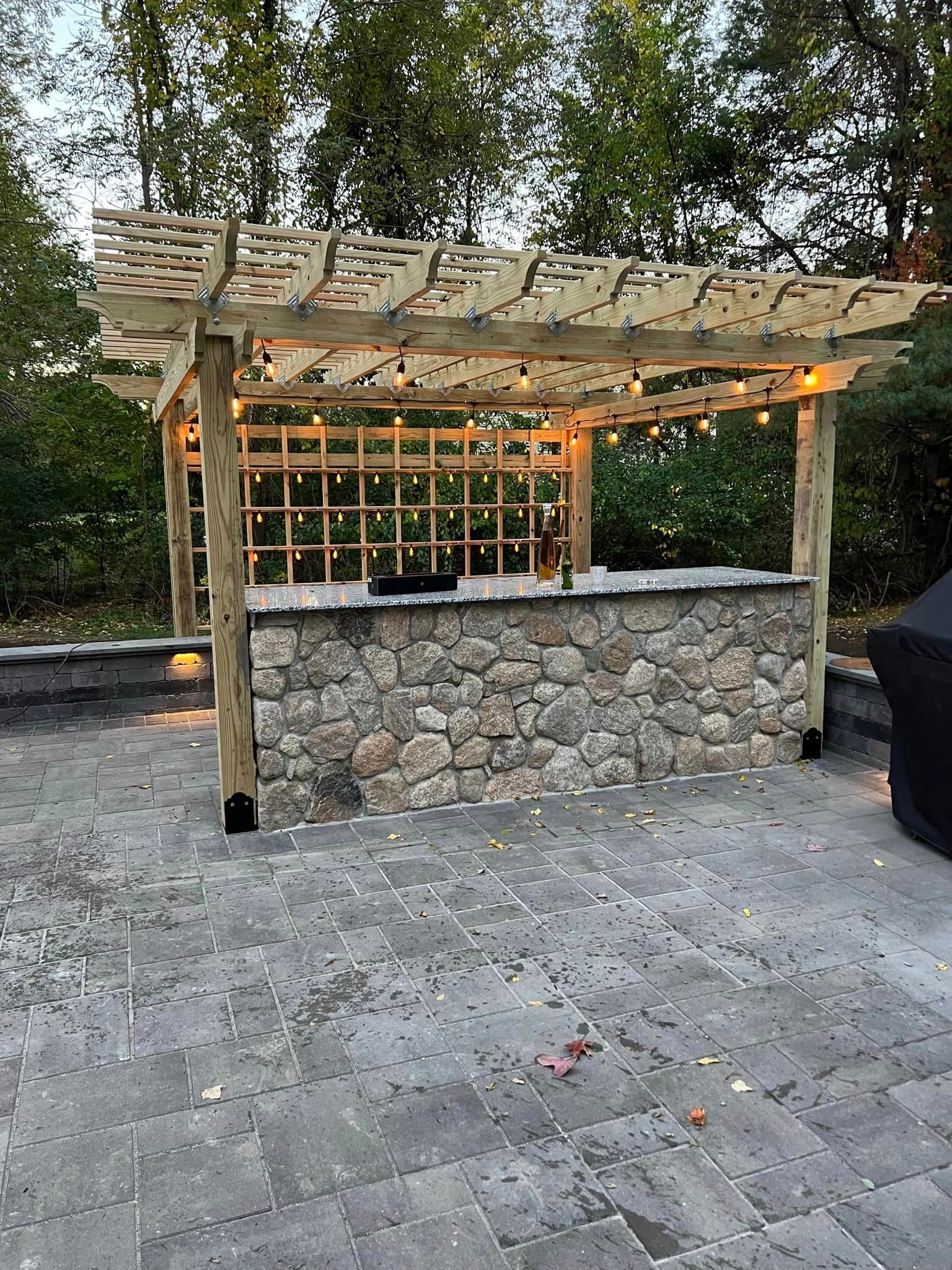 a wooden pergola over a stone bar on a patio .