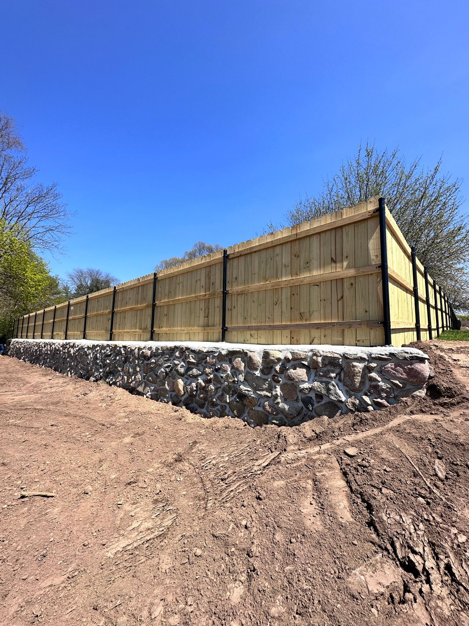 A wooden fence is sitting on top of a rock wall in a dirt field.