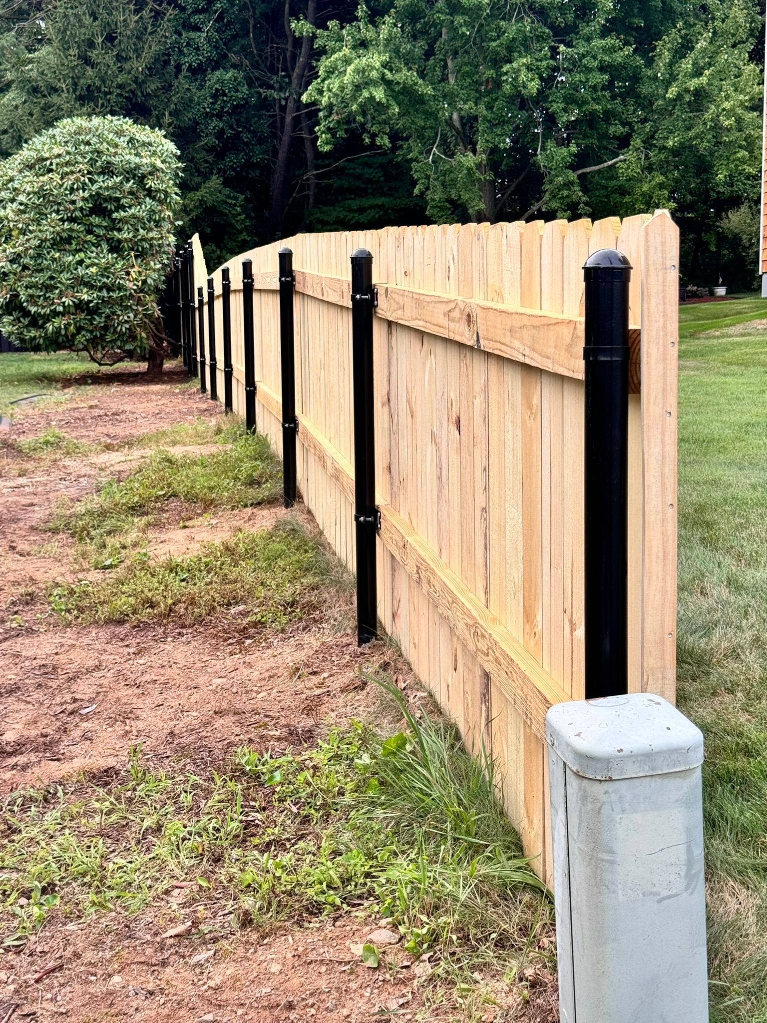 A wooden fence with black posts is sitting in the middle of a grassy field.