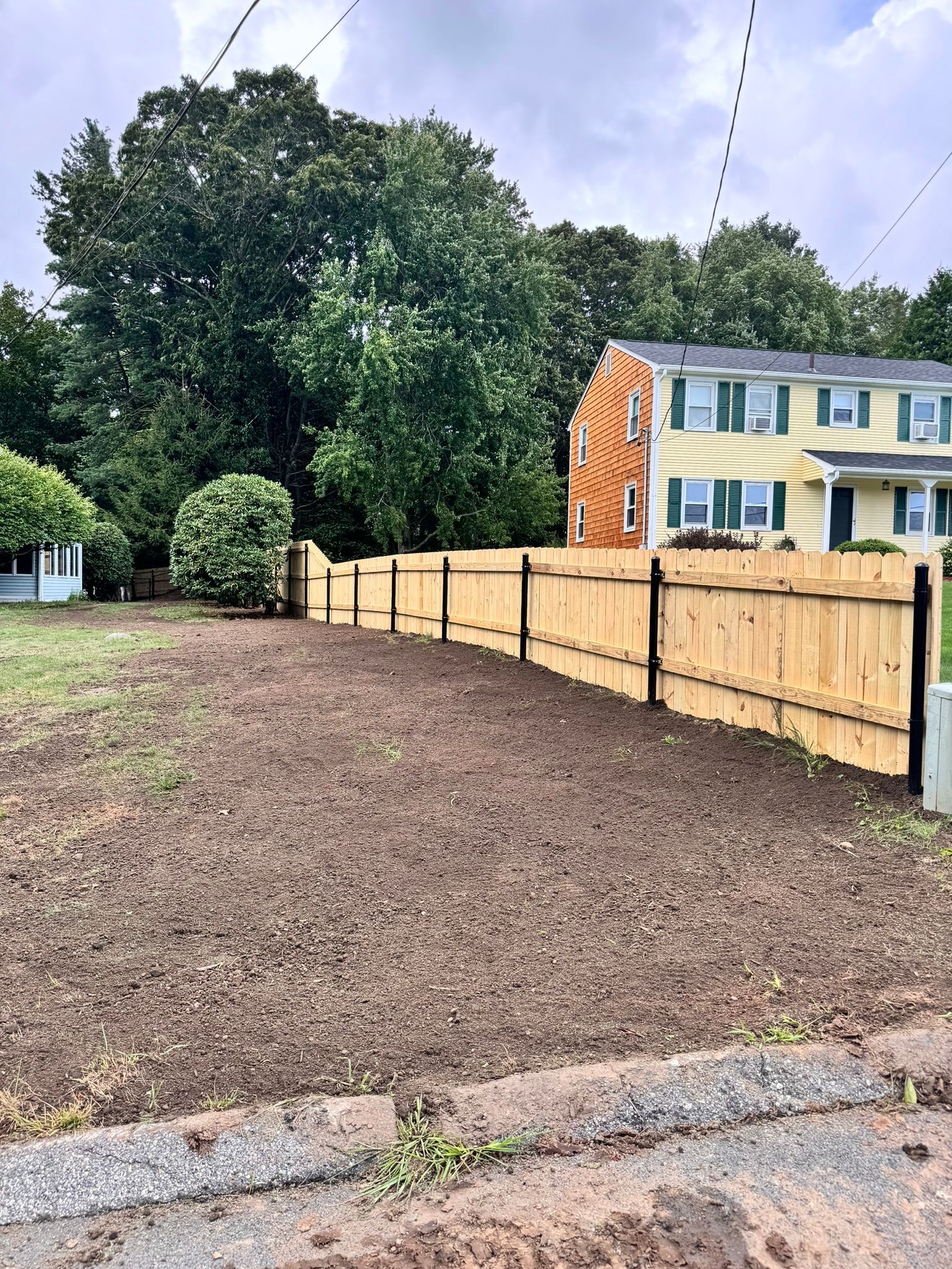 A wooden fence surrounds a dirt field in front of a house.
