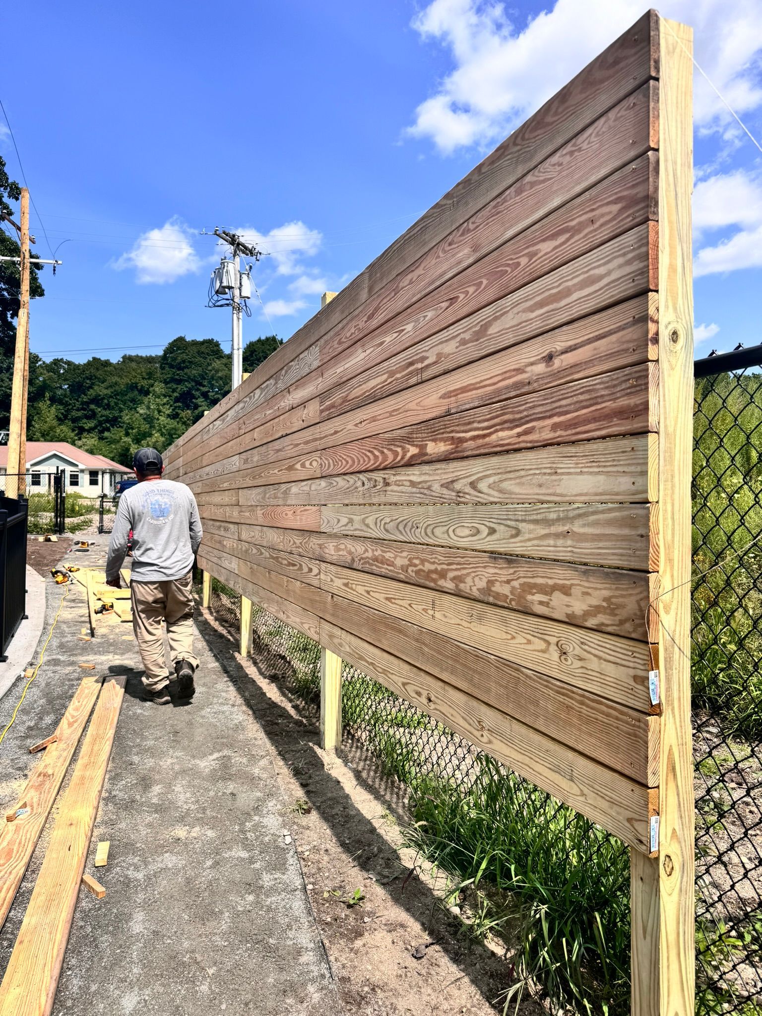 A man is walking along a wooden fence next to a chain link fence.