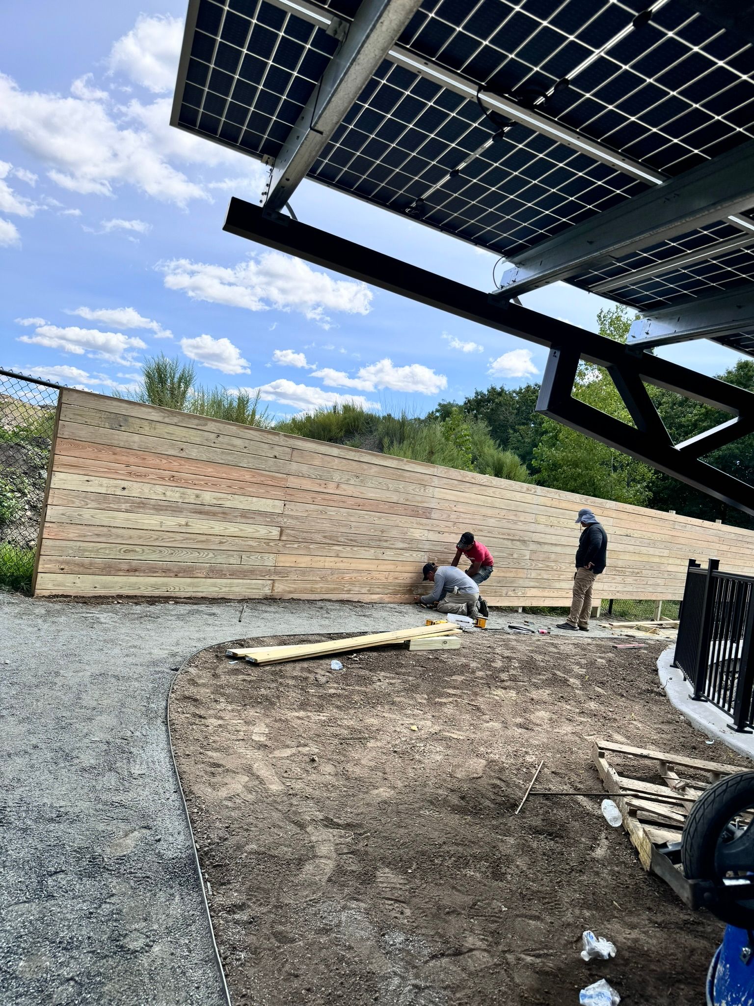A group of people are working on a wooden wall under solar panels