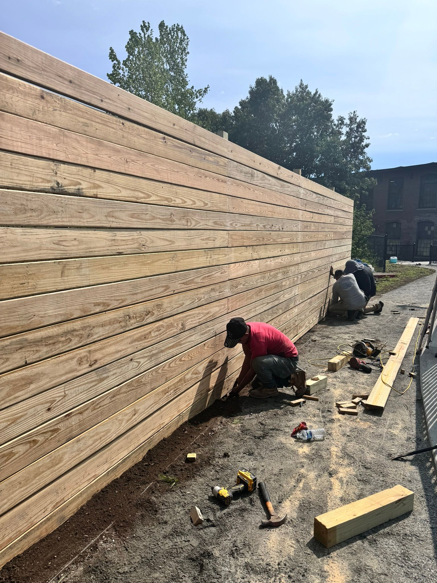A man is kneeling down next to a wooden fence.
