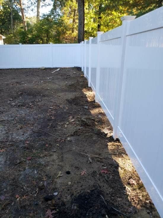 A white fence surrounds a dirt field in a backyard.