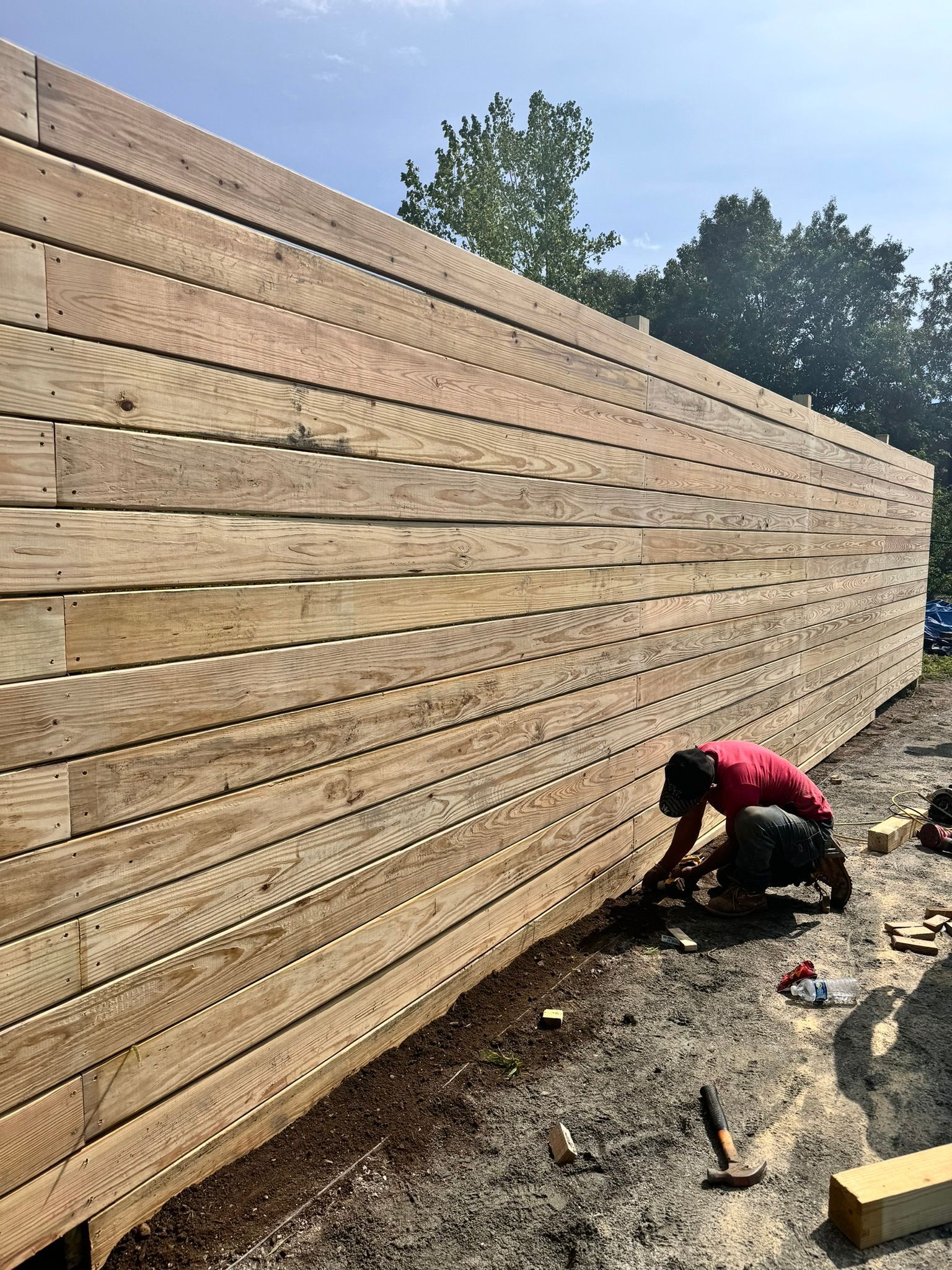 A man is working on a wooden fence in the dirt.
