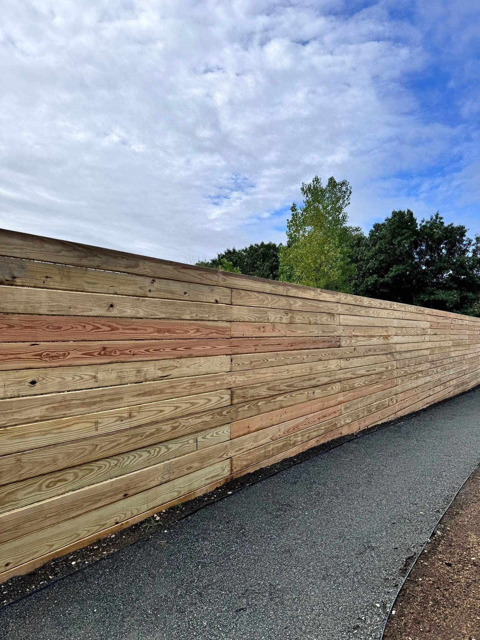A wooden fence along a gravel path with trees in the background.