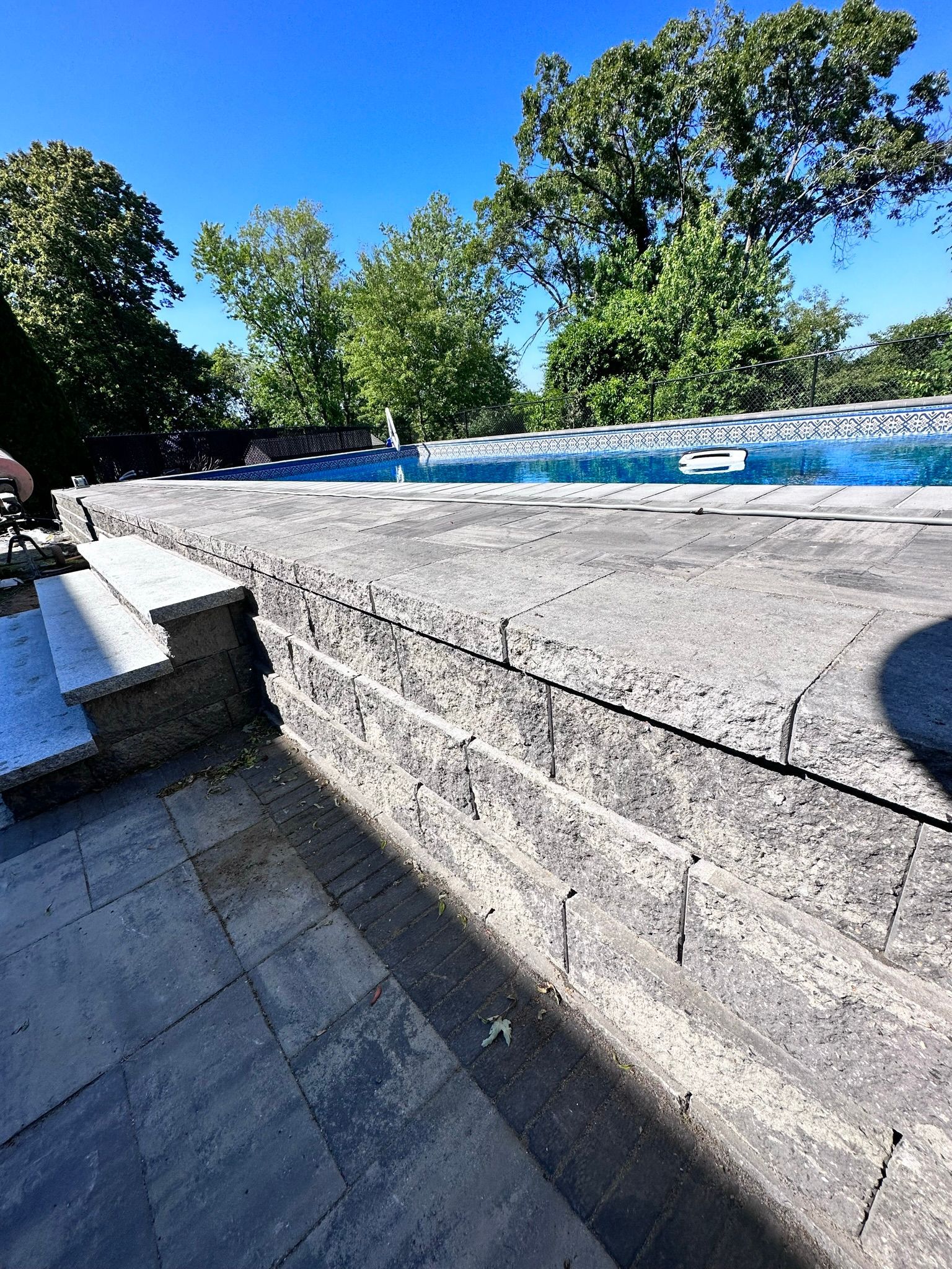 A large swimming pool is surrounded by trees and a stone wall
