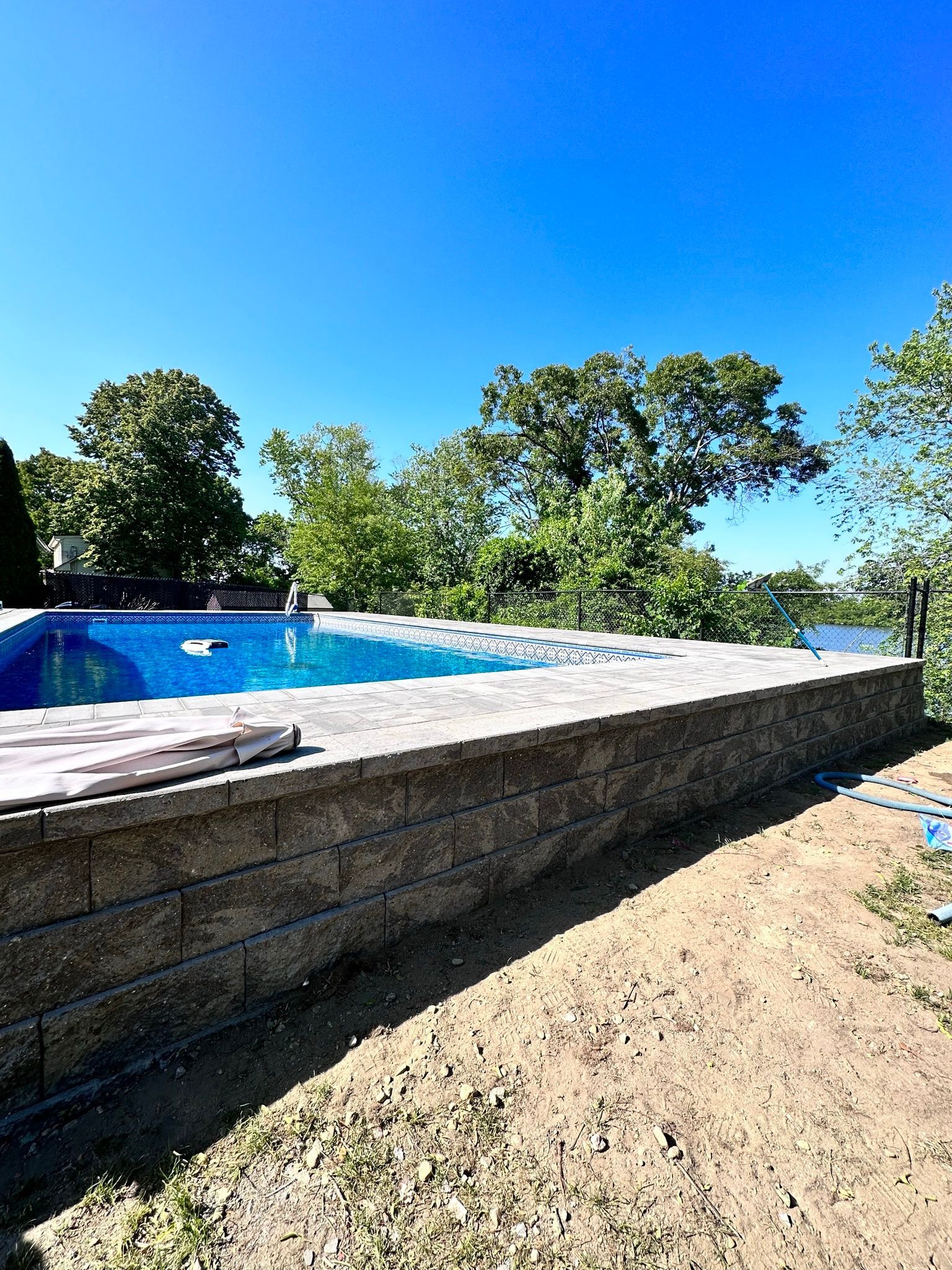 A swimming pool is surrounded by a stone wall and trees on a sunny day