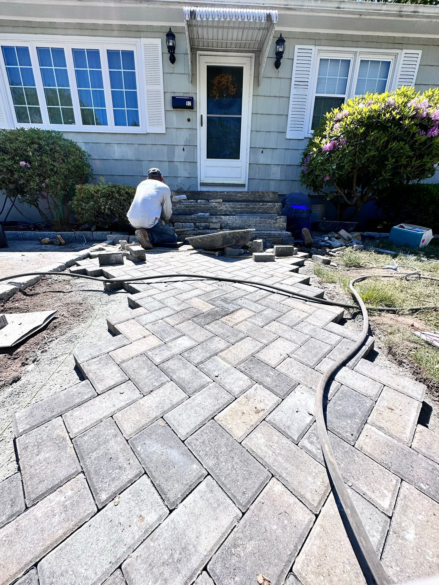 A man is working on a brick walkway in front of a house