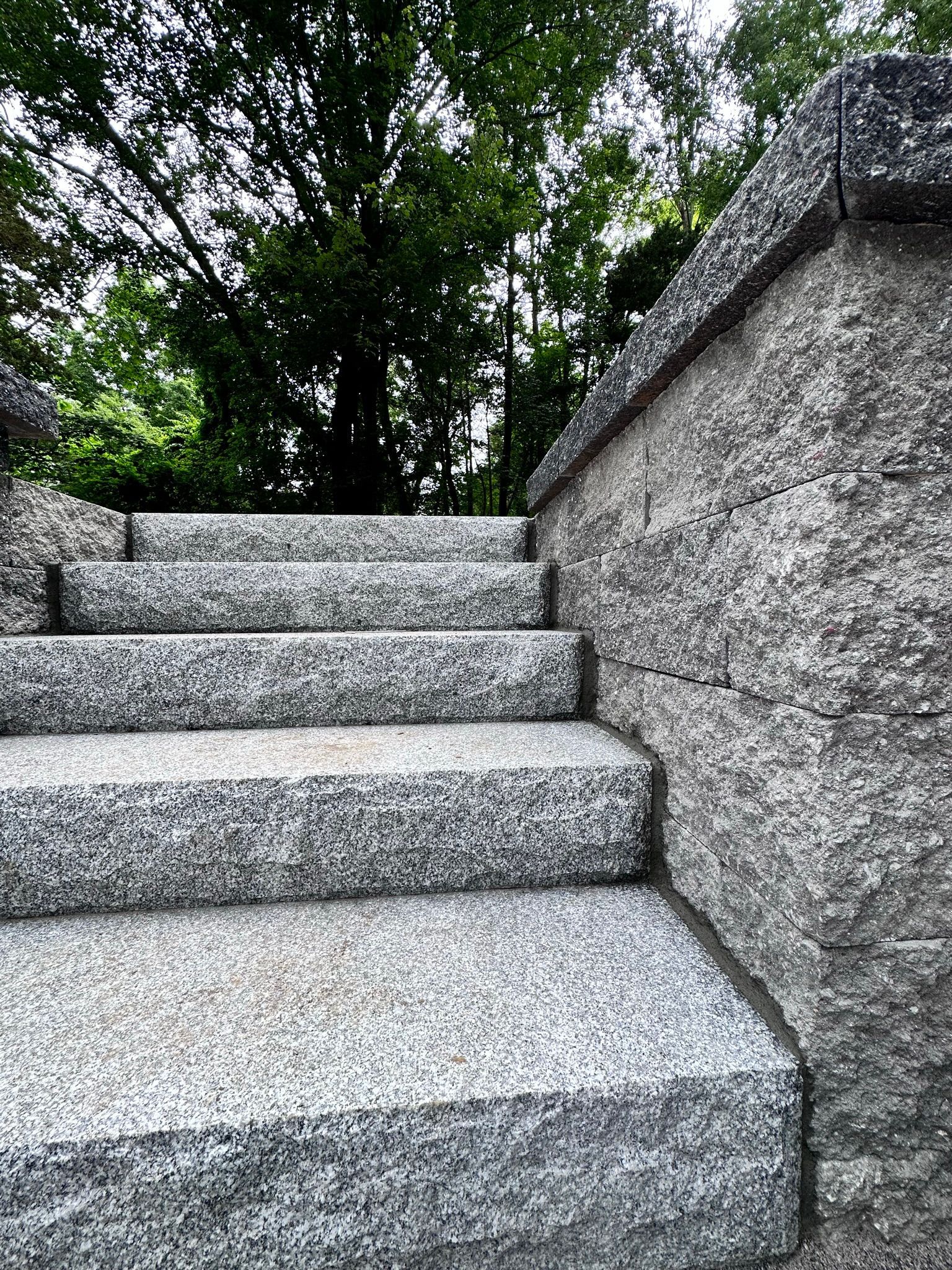 A set of stairs leading up to a stone wall with trees in the background