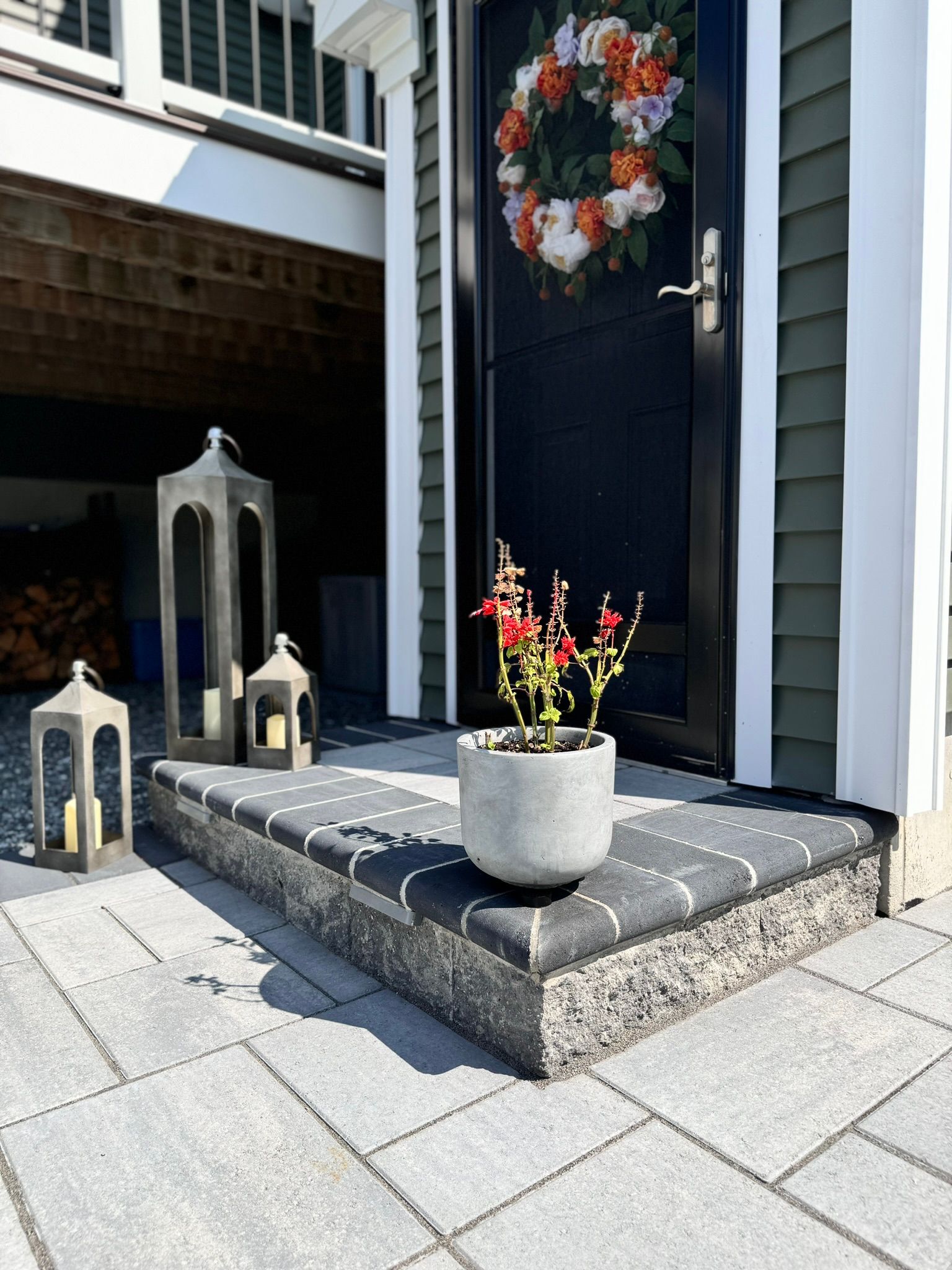 A potted plant is on the porch of a house with a wreath on the door