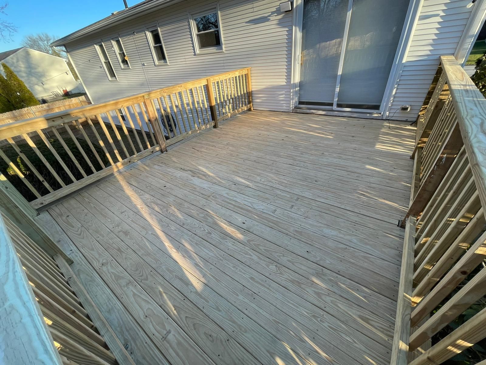 A wooden deck with a railing and a sliding glass door in front of a house.