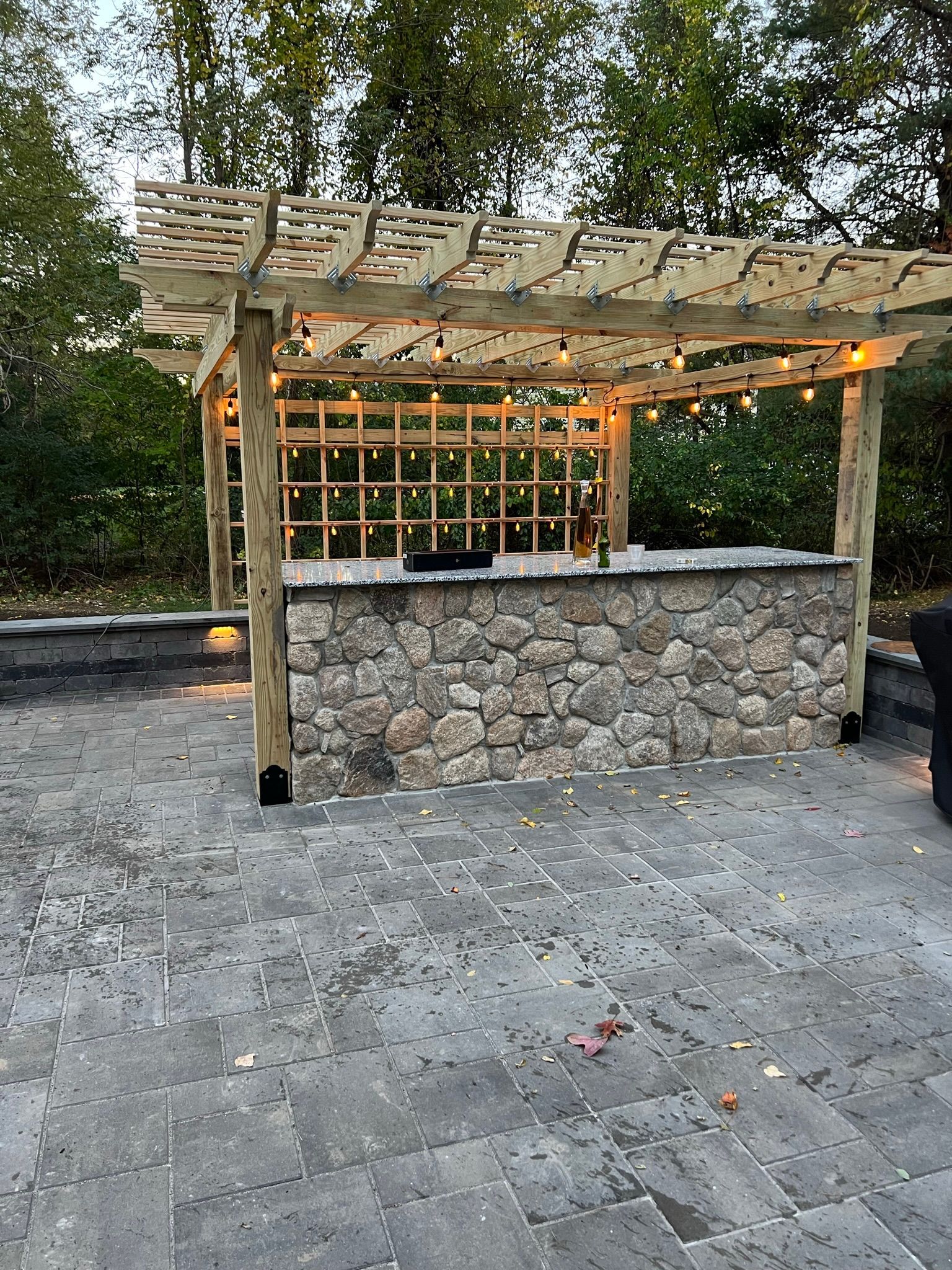 A wooden pergola over a stone bar on a patio.