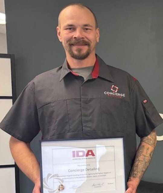 Man in gray work shirt holds a framed certificate;