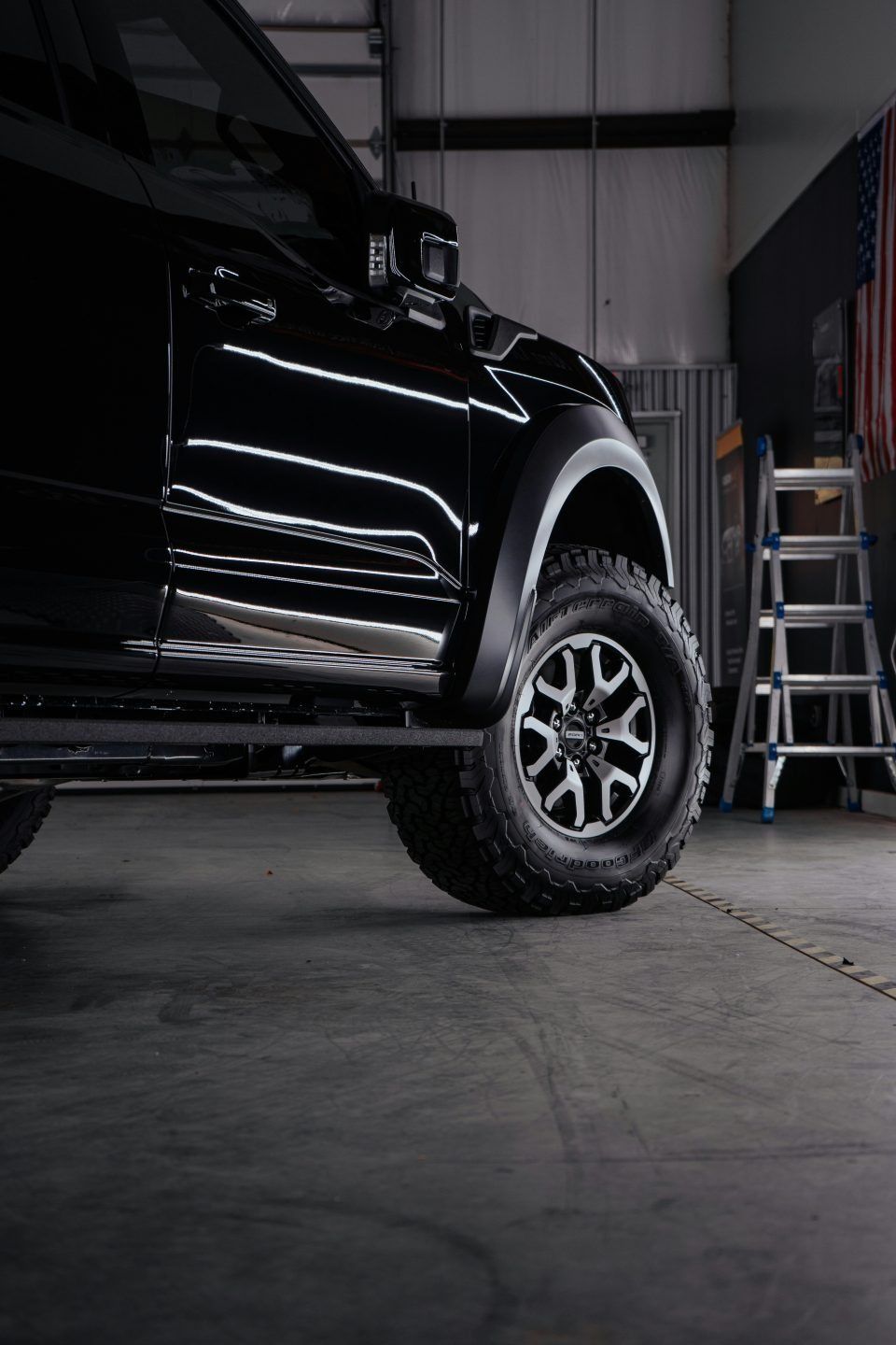 Black pickup truck wheel, shiny black paint, in a garage.