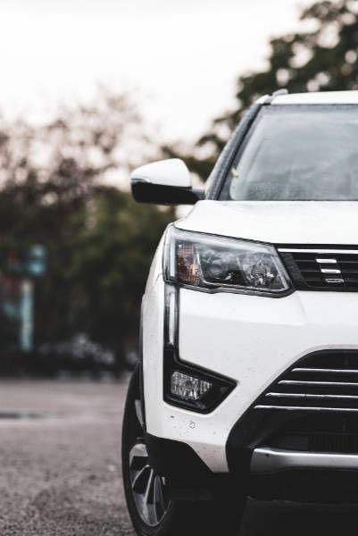 White SUV front, parked on a paved road, daytime. Trees in the background.