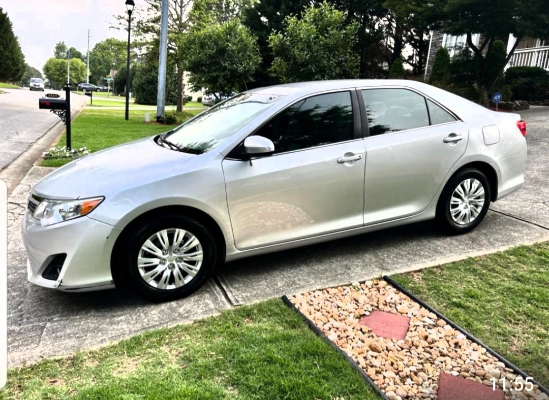 Silver Toyota Camry parked on a residential driveway, next to a mailbox and a small yard with landscaping.