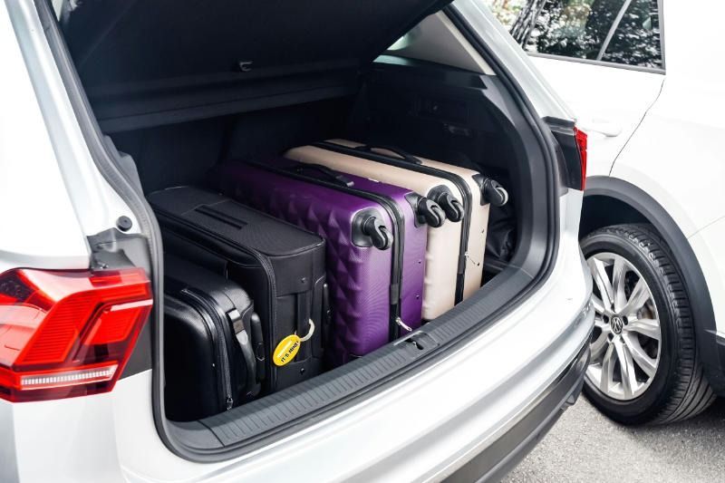 Silver car trunk filled with four suitcases: black, tan, purple, and a smaller black case.