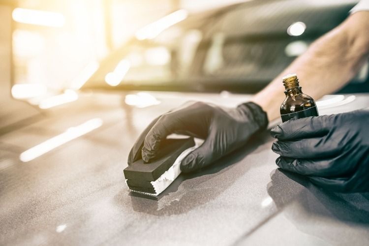 A person in black gloves applying ceramic coating to a car's hood with an applicator.
