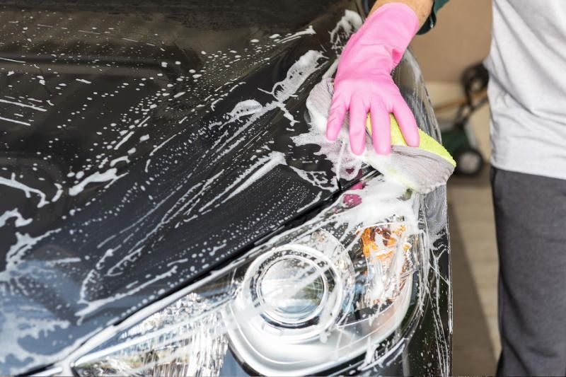 Person wearing a pink glove washing a black car with soapy water and a sponge.