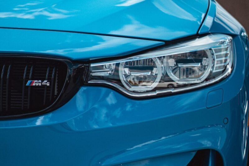 Close-up of a blue BMW M4 car headlight and grill, showing the M4 badge.