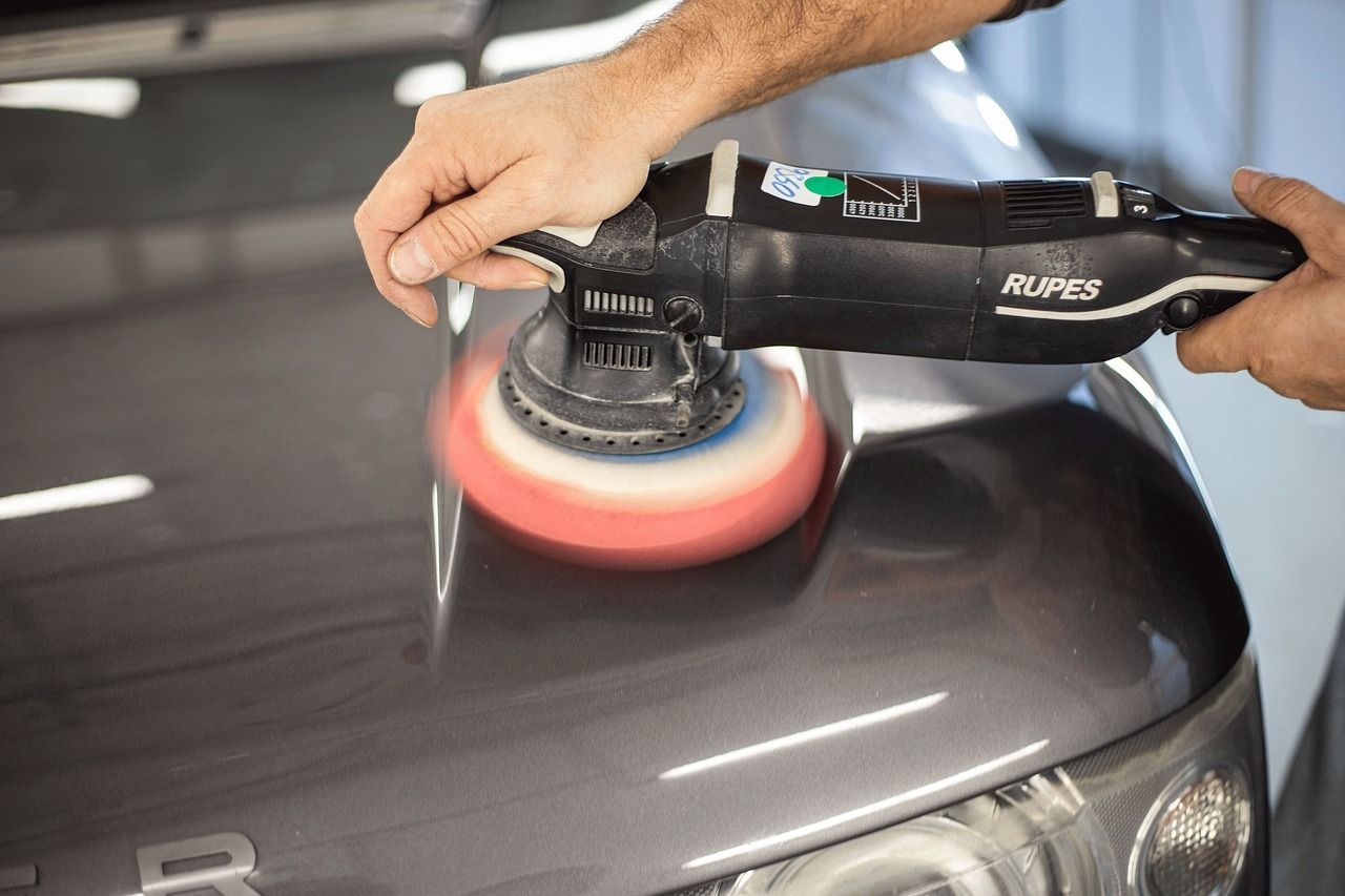 Person using a power buffer on a gray car hood.