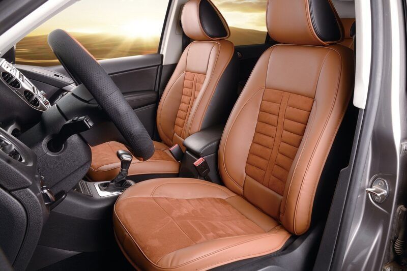 Brown and tan leather car seats with a black steering wheel, sunlit interior.
