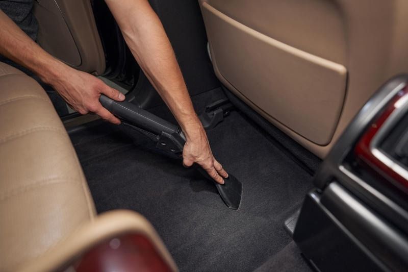 Person vacuuming a car's interior. Black vacuum nozzle cleaning a dark gray carpeted floor in a vehicle.