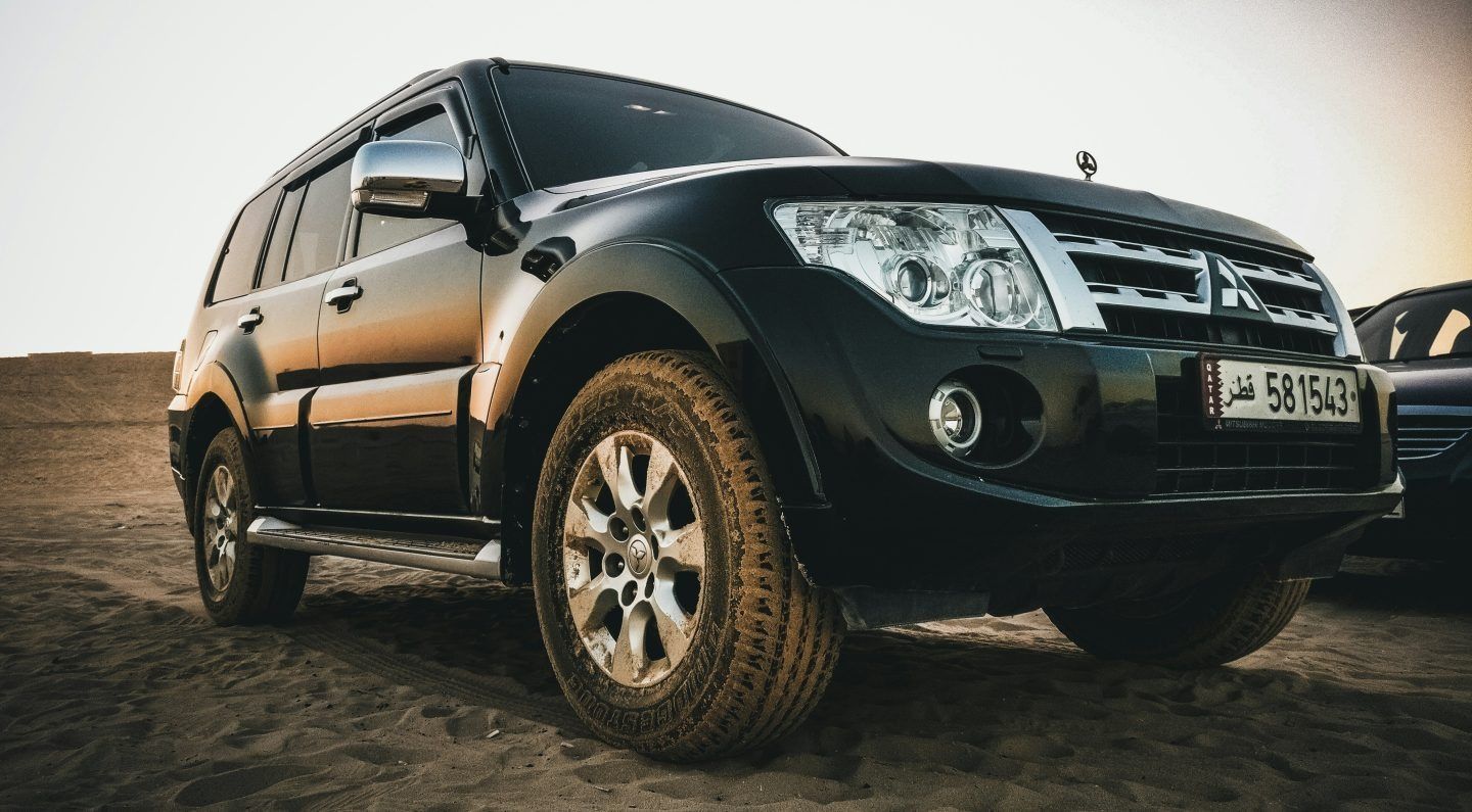 Black Mitsubishi Pajero SUV parked on sandy ground.