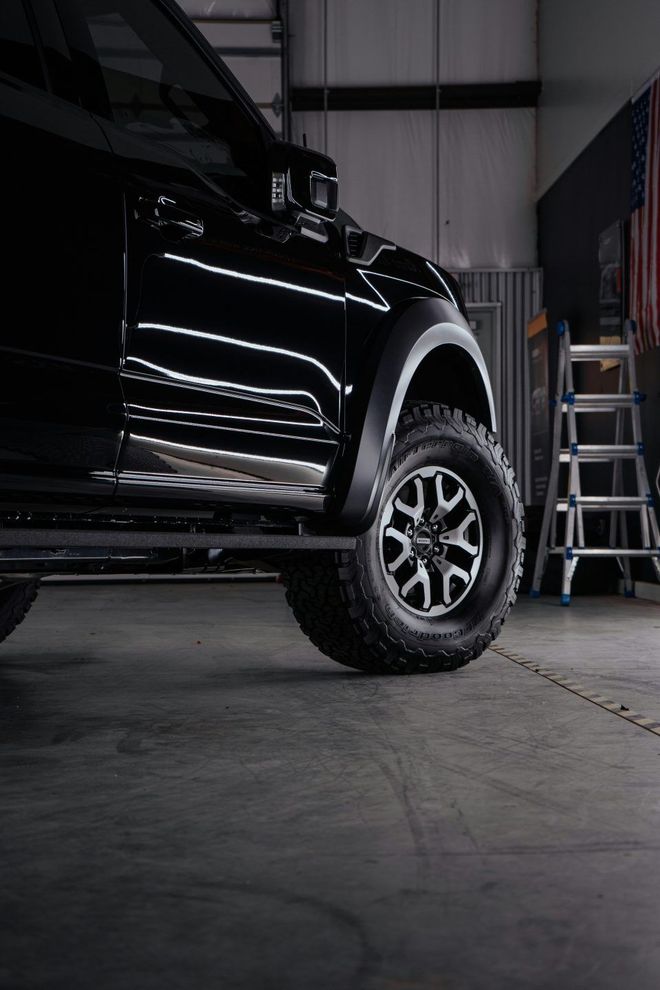 Black truck parked inside a garage; wheel and side panel visible. Gray concrete floor.
