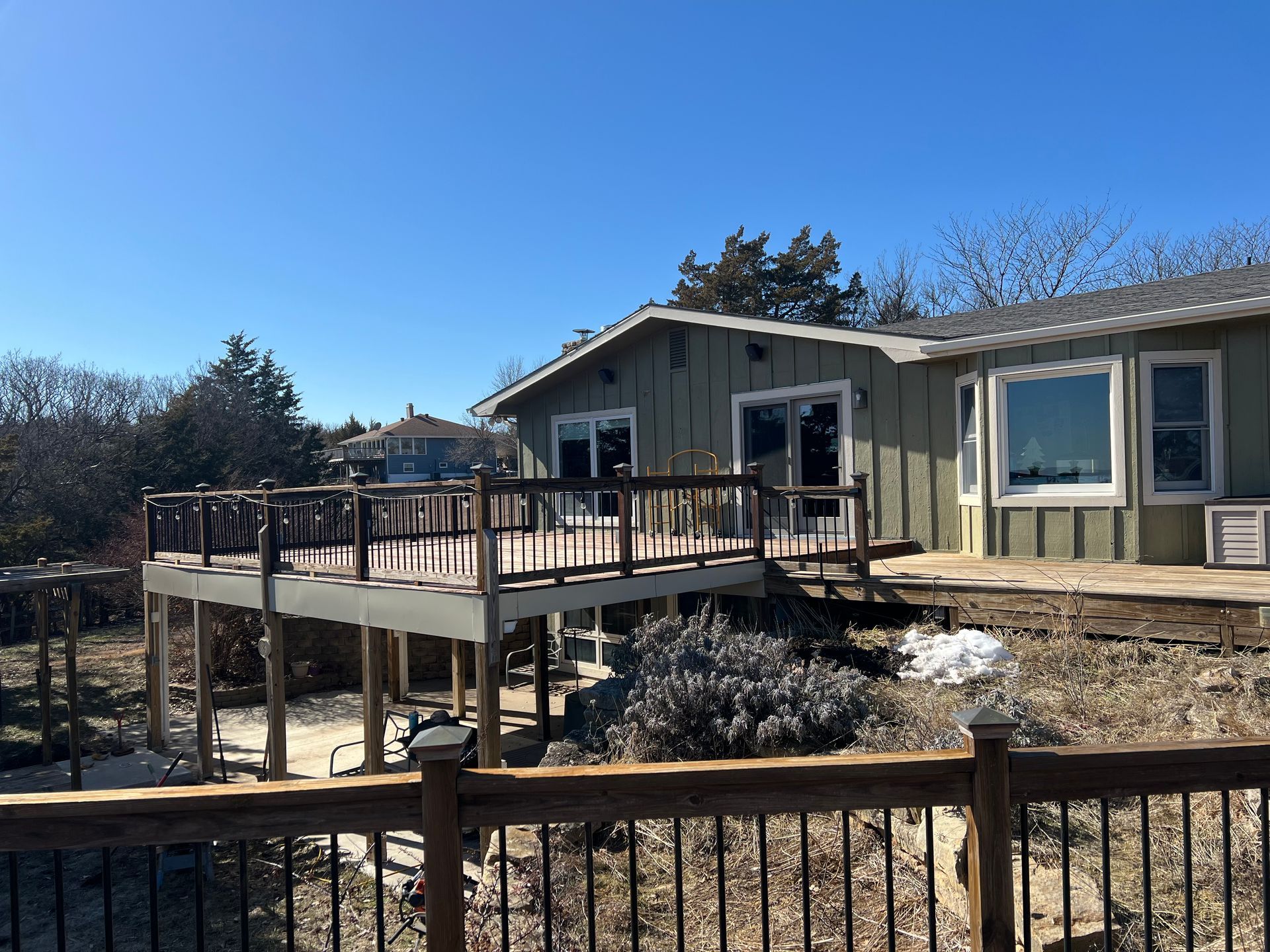 House with wooden deck, steps, and railing; blue sky, sunny day.