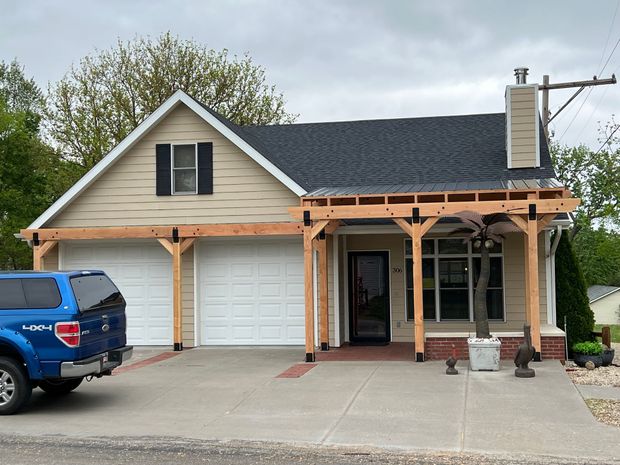Tan house with a detached garage and pergola. Blue truck parked in front.