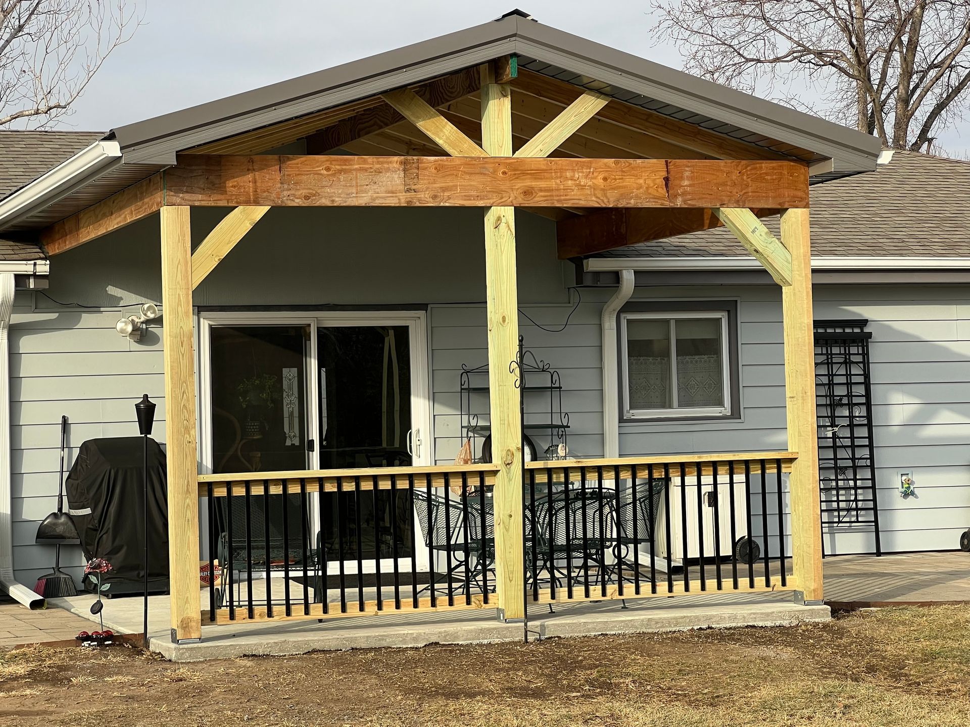 A new wooden porch addition with a black railing, covering a door and window of a light blue house.