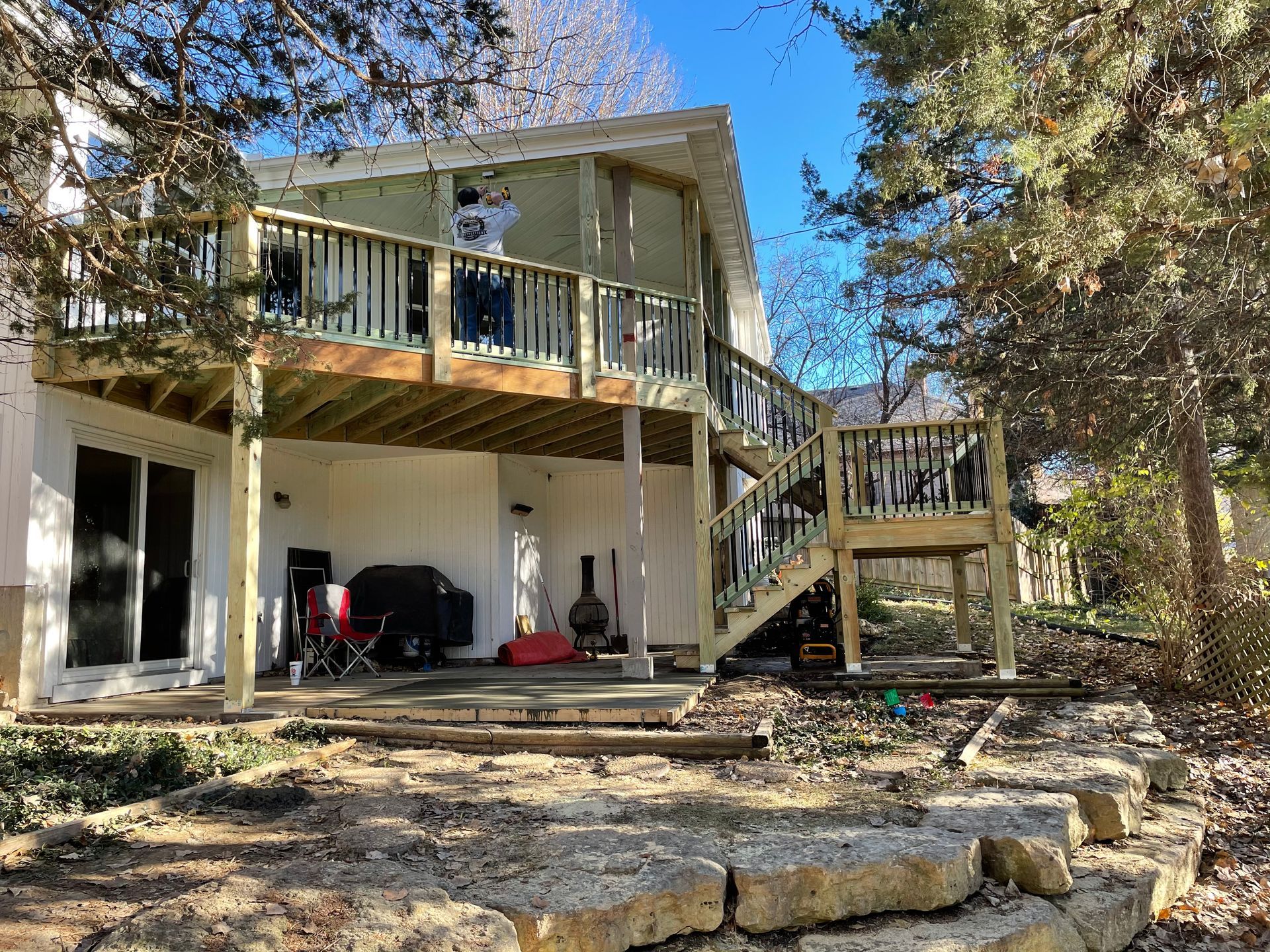 Two-story house with wooden deck, stairs, and retaining wall. Overcast day.