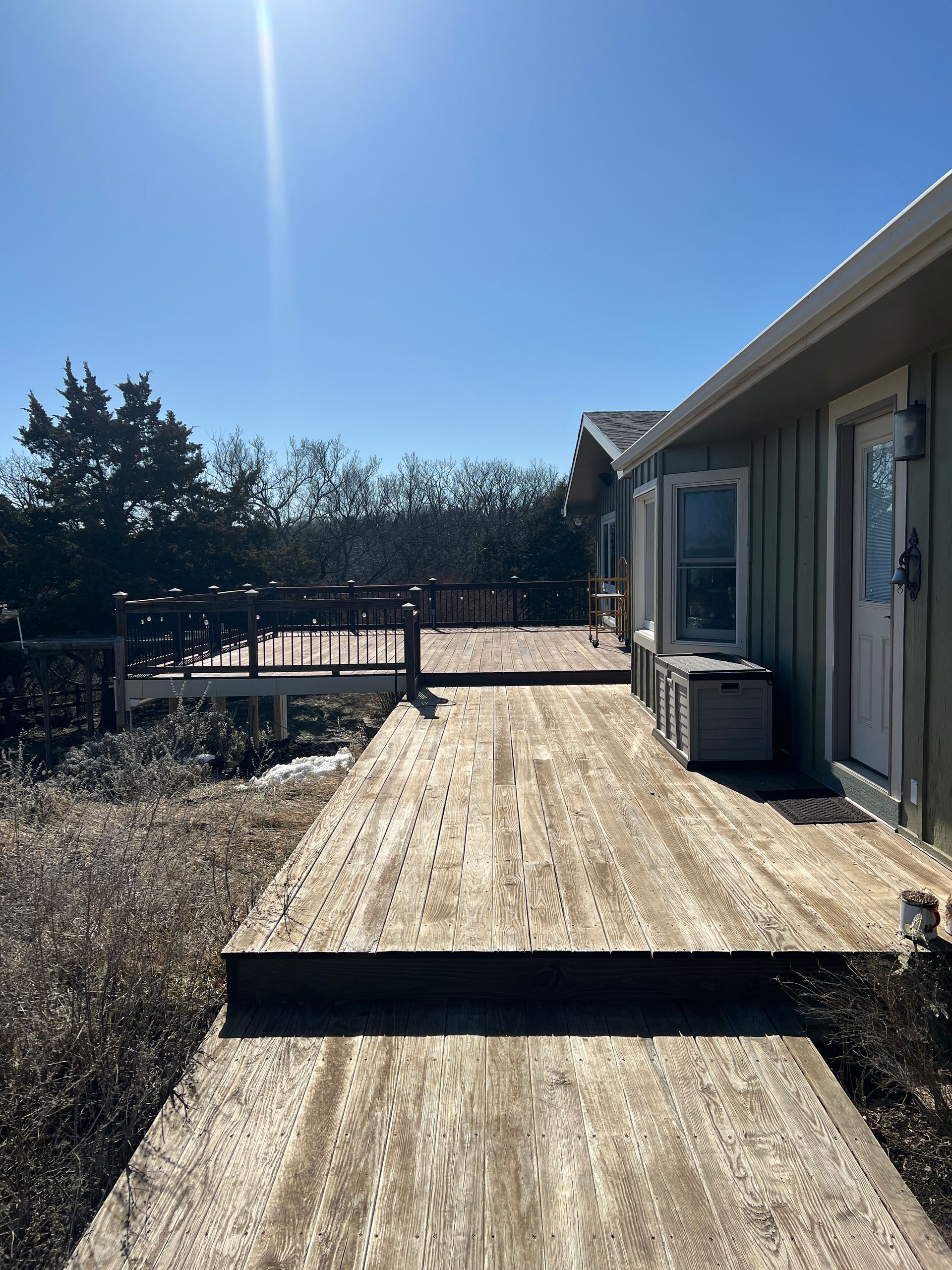 Wooden deck and walkway extending from a light green house on a sunny day.