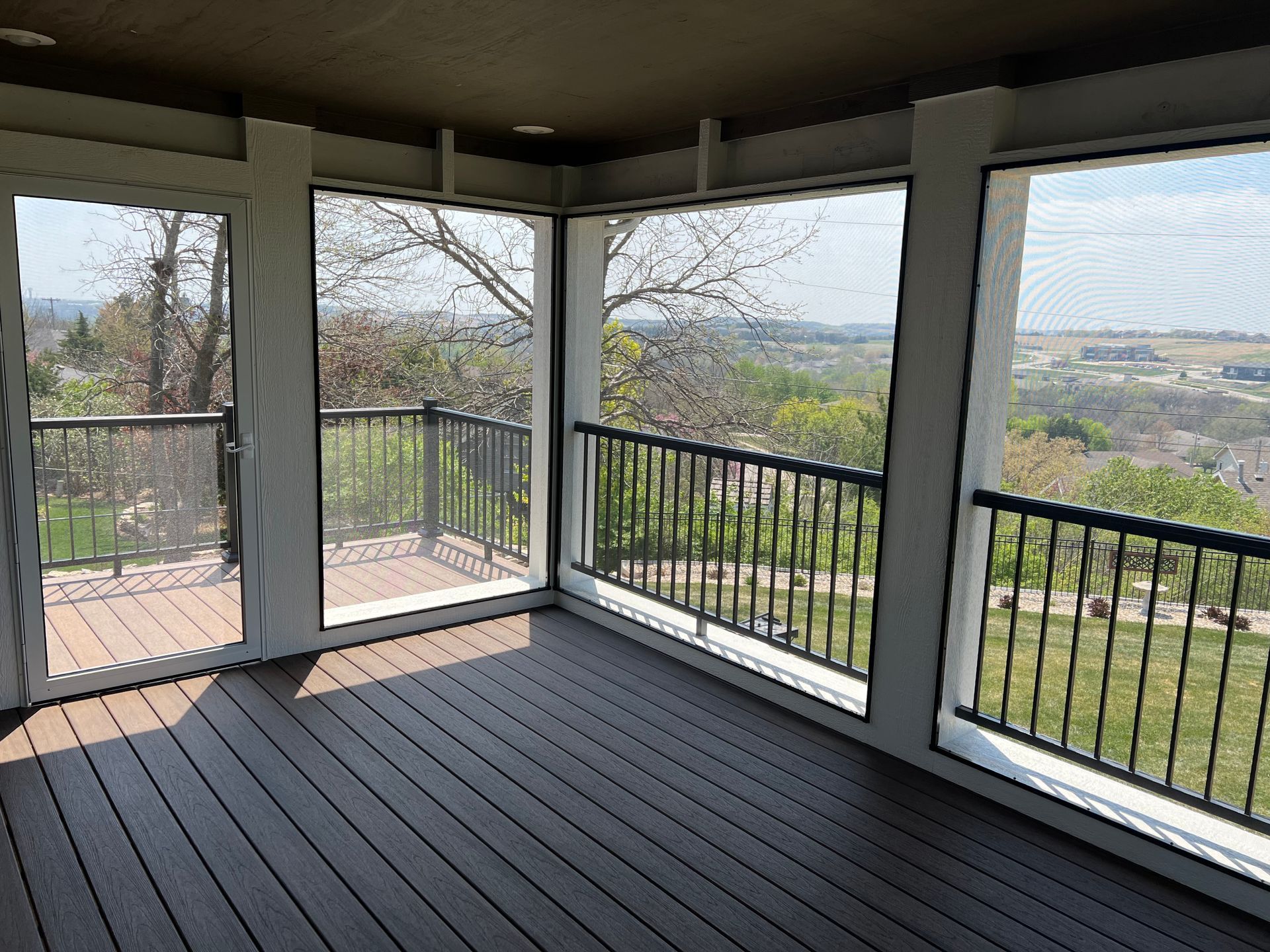 Screened porch with dark wood deck, black railing, and scenic view of trees and landscape.