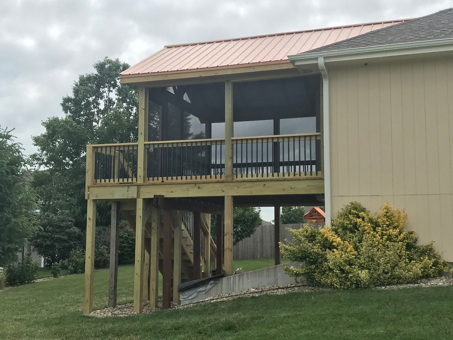 Screened-in wooden deck with black railings, tan siding, and copper-colored roof. Set in grassy yard.