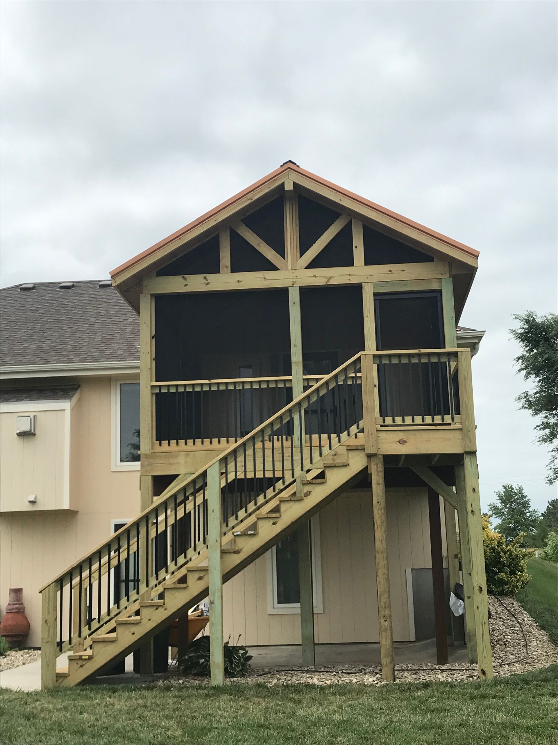 Wooden screened-in deck with stairs attached to a two-story beige house, under a cloudy sky.