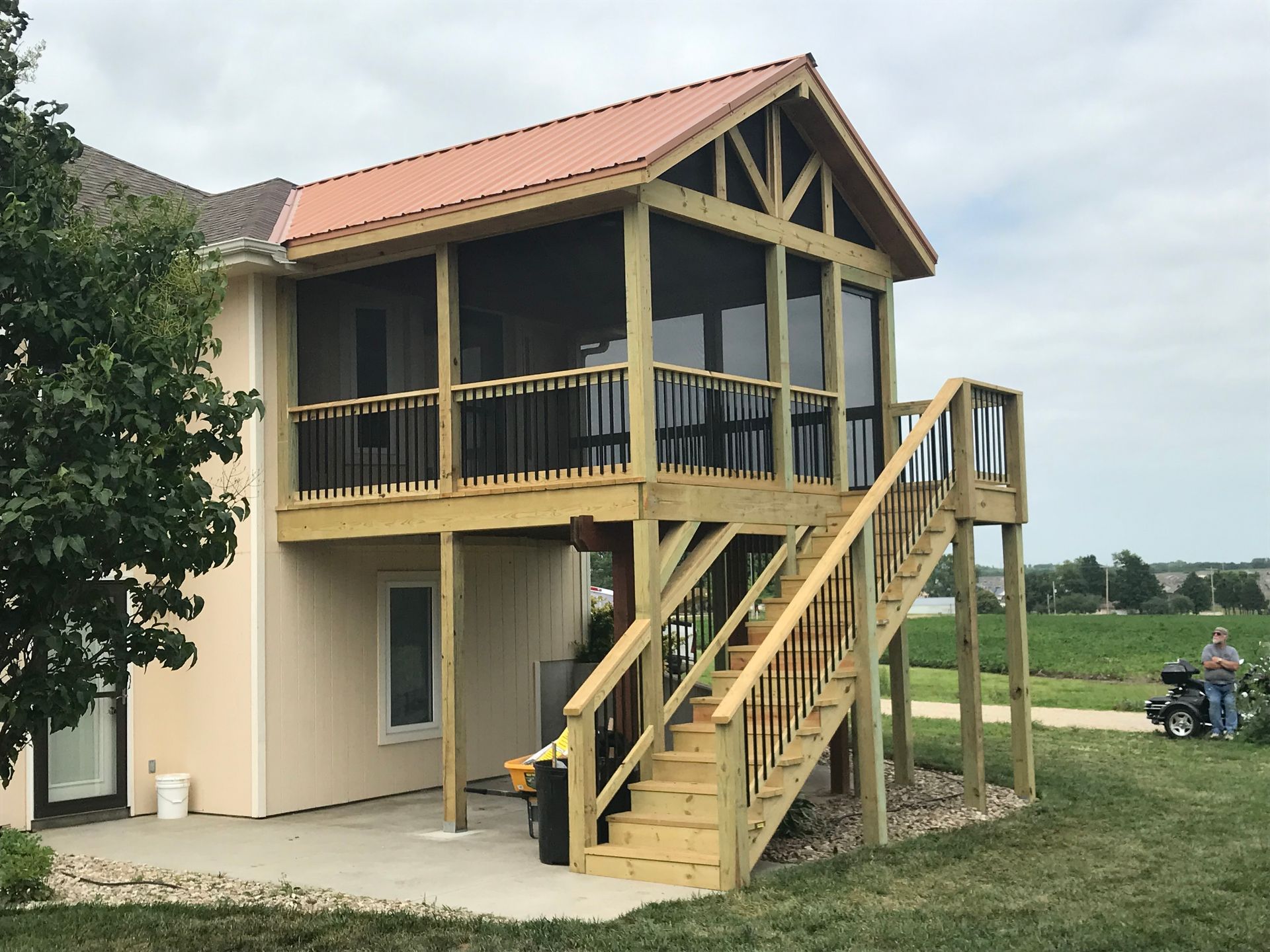Wooden screened porch with staircase attached to a beige house, with a metal roof.