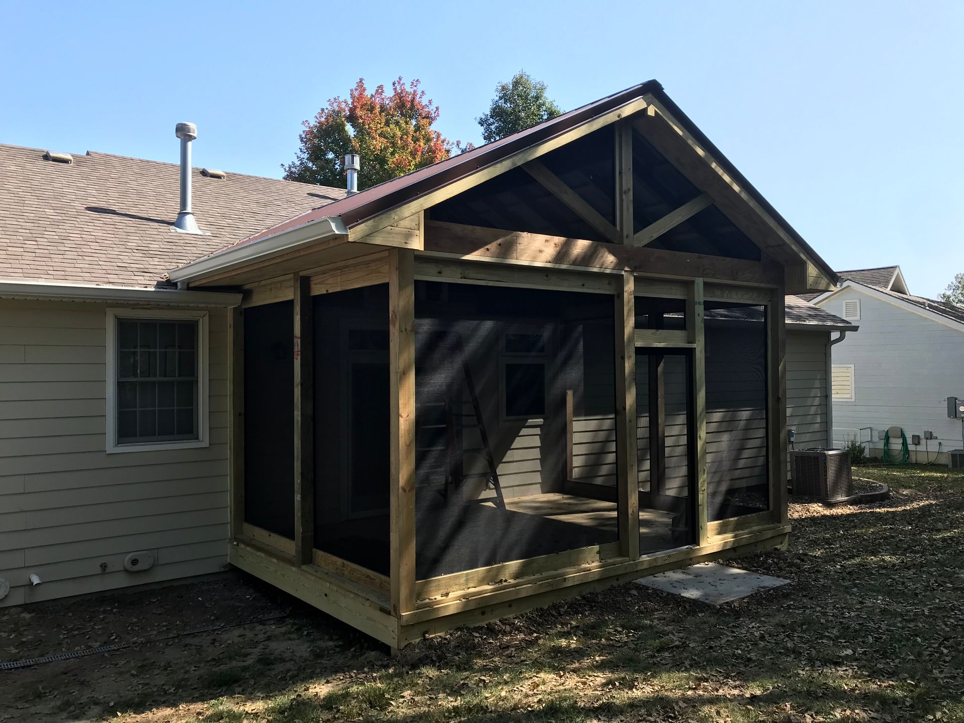 Screened-in porch attached to a house; wooden frame with dark screens, brown roof, and deck.