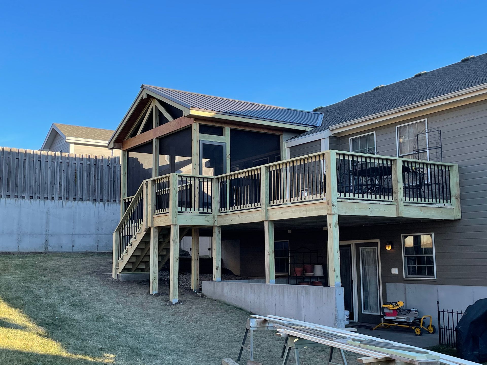Wooden deck with screened-in porch attached to a beige house, steps leading to a yard, clear sky.
