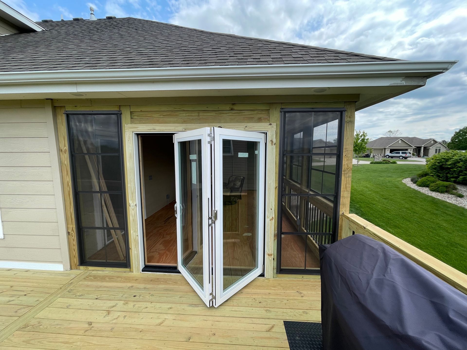 A screened porch with French doors opening onto a wooden deck, next to a grassy yard.